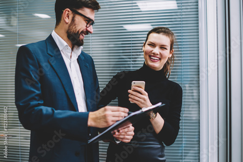 Young skilled man and woman entrepreneurs dressed in formal wear making jokes and sincerely laughing while working together.Successful employees having fun during collaboration in modern office photo