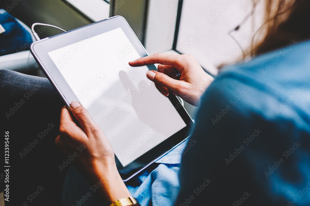 Obraz premium Rear view of young woman touching with finger on blank screen area of digital touch pad to choosing music application for installing on device via public wireless transport internet sitting in tram