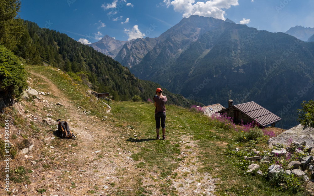 Fototapeta premium Hiker photographing alpine peaks near rustic cabin mountain landscape