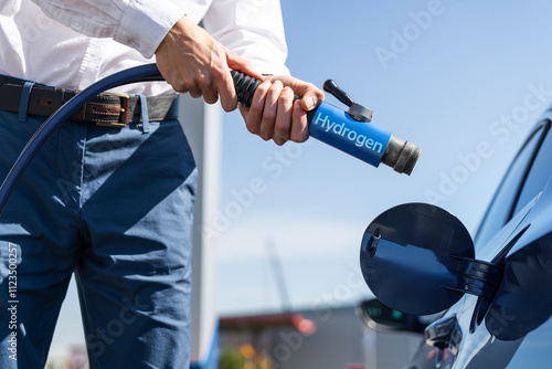 Man holds a hydrogen fueling nozzle on a hydrogen filling station. Refueling car with hydrogen fuel.	 photo