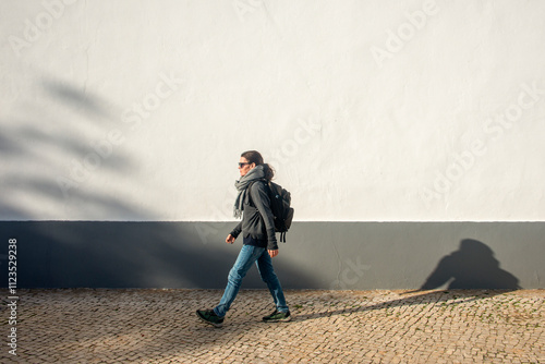 woman with a backpack walking by a white wall, exercise.