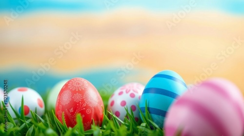 Colorful Easter eggs arranged on grass with a blurred beach background during...