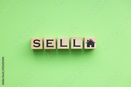 SELL text and house icon written on wooden blocks on green background. 