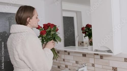 Woman in a bathrobe arranges roses in a bath sink in a bright bathroom, showcasing a serene morning routine in slow motion