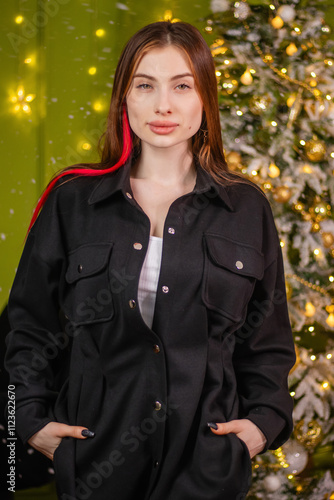 Portrait of a young woman in a black suit posing standing against the backdrop of a Christmas tree.