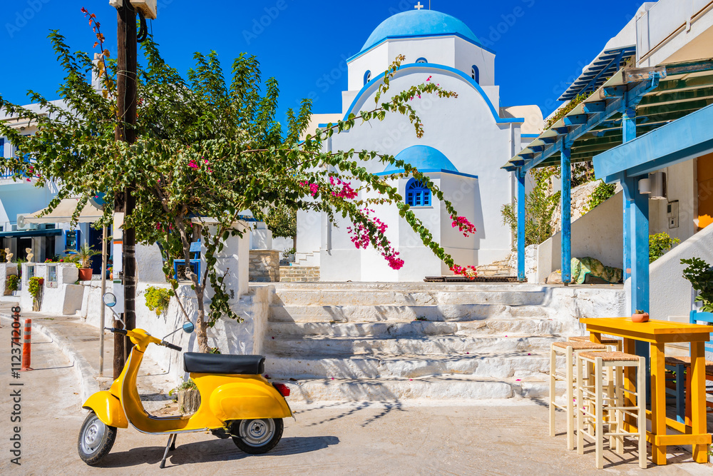 Yellow scooter and traditional Greek style white church in Apollonas village, Naxos island, Cyclades, Greece