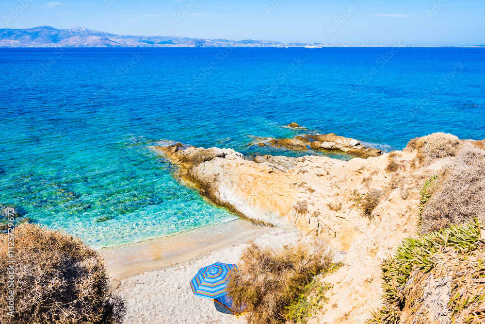 Sun umbrella on idyllic sandy beach with rocks in sea water near Orkos bay, Naxos island, Cyclades, Greece
