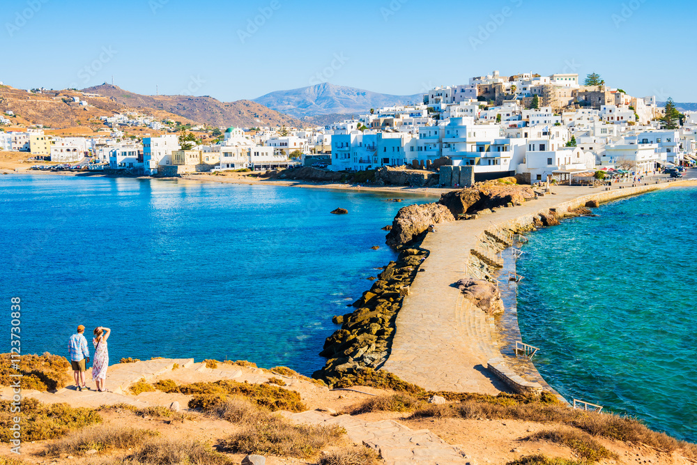 Couple of unidentified tourists looking at Naxos port and sea coast from Portara hill, Naxos island, Cyclades, Greece