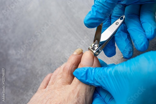 A woman in gloves trims an old woman's toenails with nail clippers. Nail care for the elderly. photo