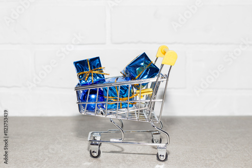 Shopping cart with New Year gifts against white brick wall. New Year and Christmas.