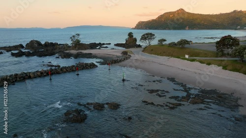 Coastal scene at sunset. Rocky shoreline with markers, calm water, and a sandy beach. Natural beauty. , KUAOTUNU, COROMANDEL PENINSULA, NEW ZEALAND photo