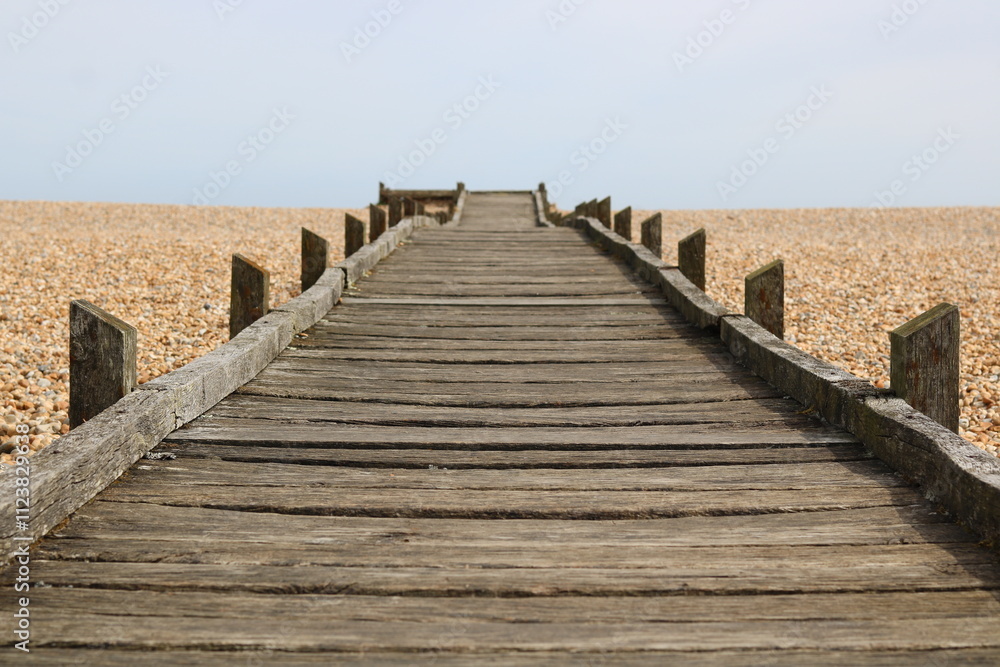Obraz premium Wooden walkway leading across pebble beach to sea in the distance