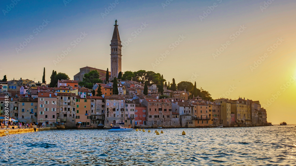 Fototapeta premium As the sun dips below the horizon, Rovinj Croatia waterfront comes alive with warm hues, showcasing colorful buildings, a towering church, and tranquil waters inviting exploration 