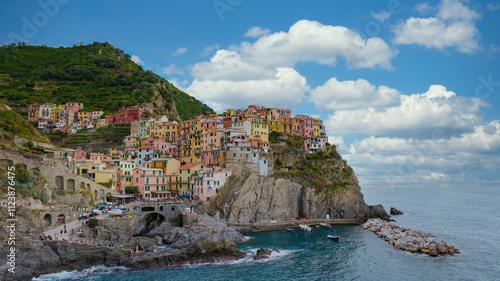 Wander through the vibrant streets of Manarola as the sun breaks through clouds, illuminating the colorful homes perched on cliffs, overlooking the tranquil sea in picturesque Cinque Terre Italy