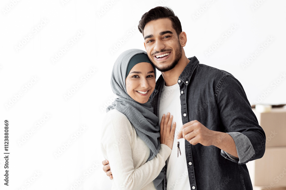 Obraz premium Happy muslim family standing over paper boxes and showing keys from their new apartment. Handsome arab man and young woman in hijab moving to their house, unpacking belongings, copy space