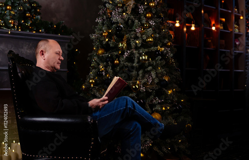 man sits comfortably in a chair in the living room, engrossed in a book while the festive Christmas tree glows nearby, creating a cozy atmosphere.