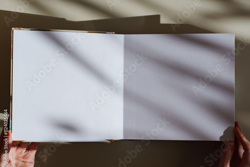 Female hands flipping through a photo book with white pages on a white table.  photo