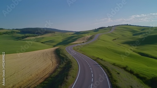 Endless Asphalt Road Winding Through Lush Rolling Green Hills Under a Clear Blue Sky Creating a Serene and Picturesque Landscape Ideal for Travel and Nature Photography