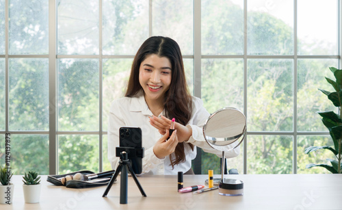 A woman filming her makeup tutorial in a bright room with large window, using a smartphone mounted on a tripod, various makeup product are on the table. photo