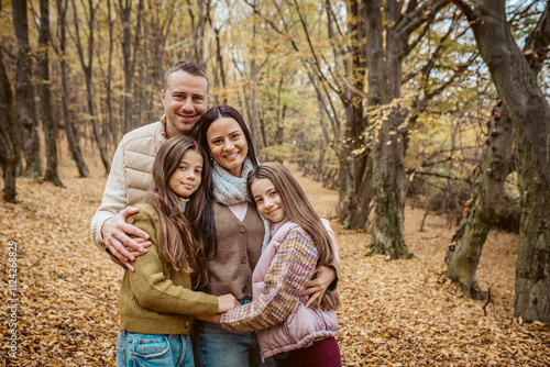 Family portrait of parents with two daughter, standing in the middle of forest.