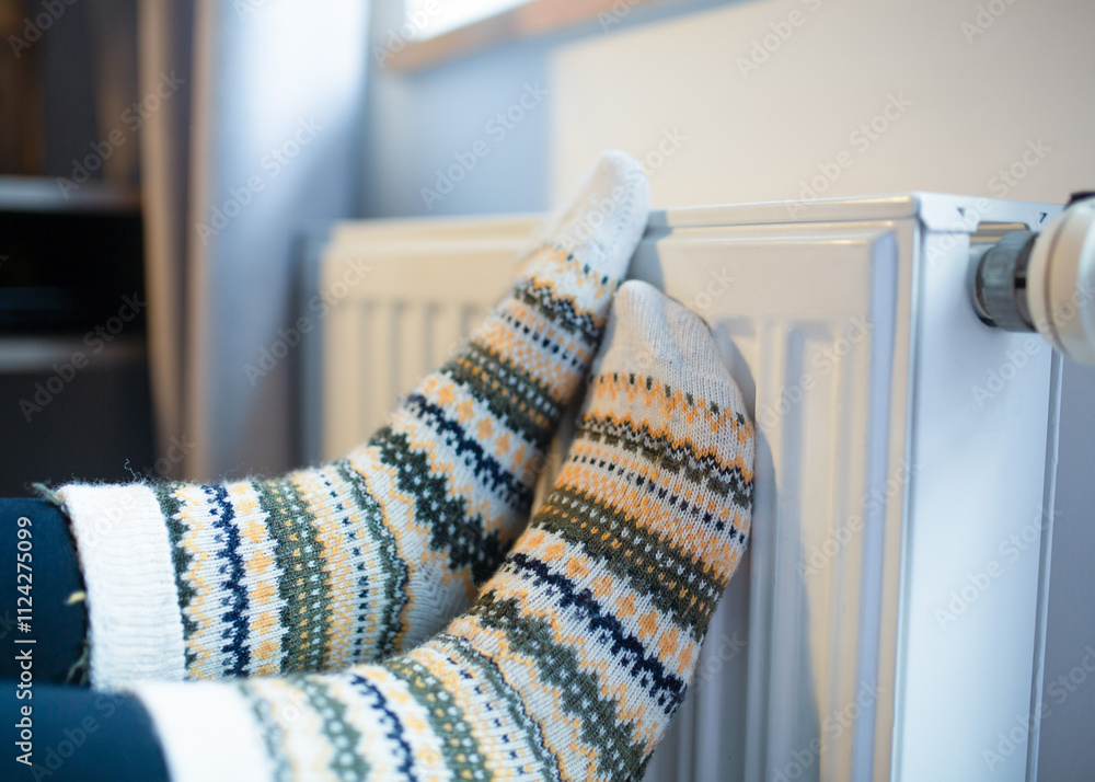 © Yuliya - Woman with her feet resting on a radiator to warm them up by the cold of winter and energy saving. © Yuliya - Woman with her feet resting on a radiator to warm them up by the cold of winter and energy saving.