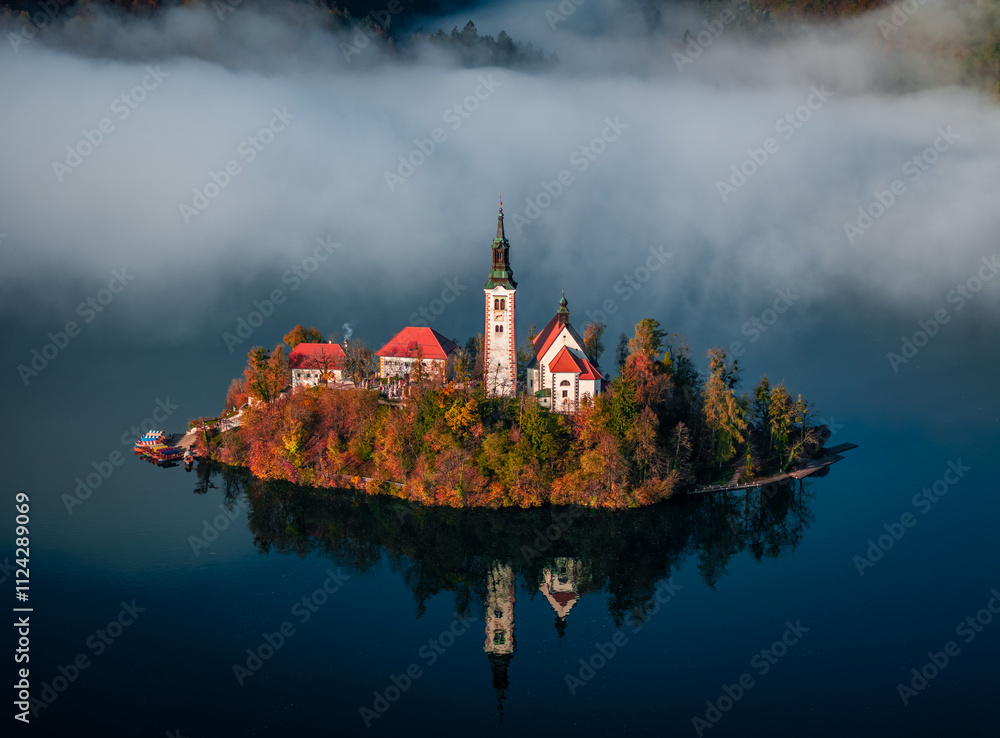 Bled, Slovenia - Beautiful foggy autumn sunrise at Lake Bled with the famous Pilgrimage Church of the Assumption of Maria (Bled Island) with heavy fog behind on an October morning