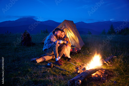 Φωτογραφία Couple hikers enjoys cozy moment by campfire, sipping hot drinks near glowing tent