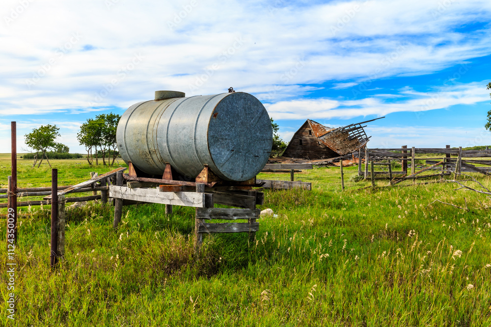 A large metal tank is sitting in a field next to a barn A large metal tank is sitting in a field next to a barn