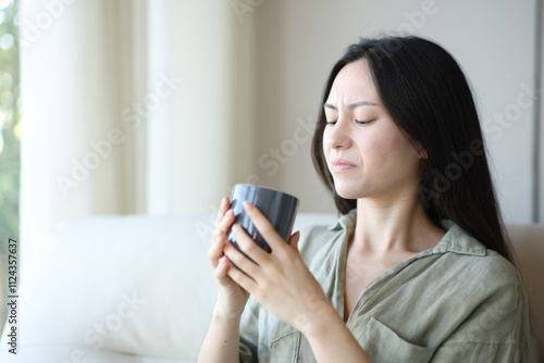 Disgusted asian woman drinking coffee