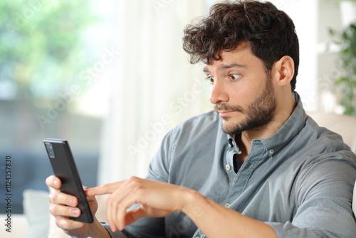 Perplexed man checking cell phone at home