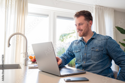 working at home in the kitchen. caucasian male sitting at the kitchen counter behind his laptop working and communicating.