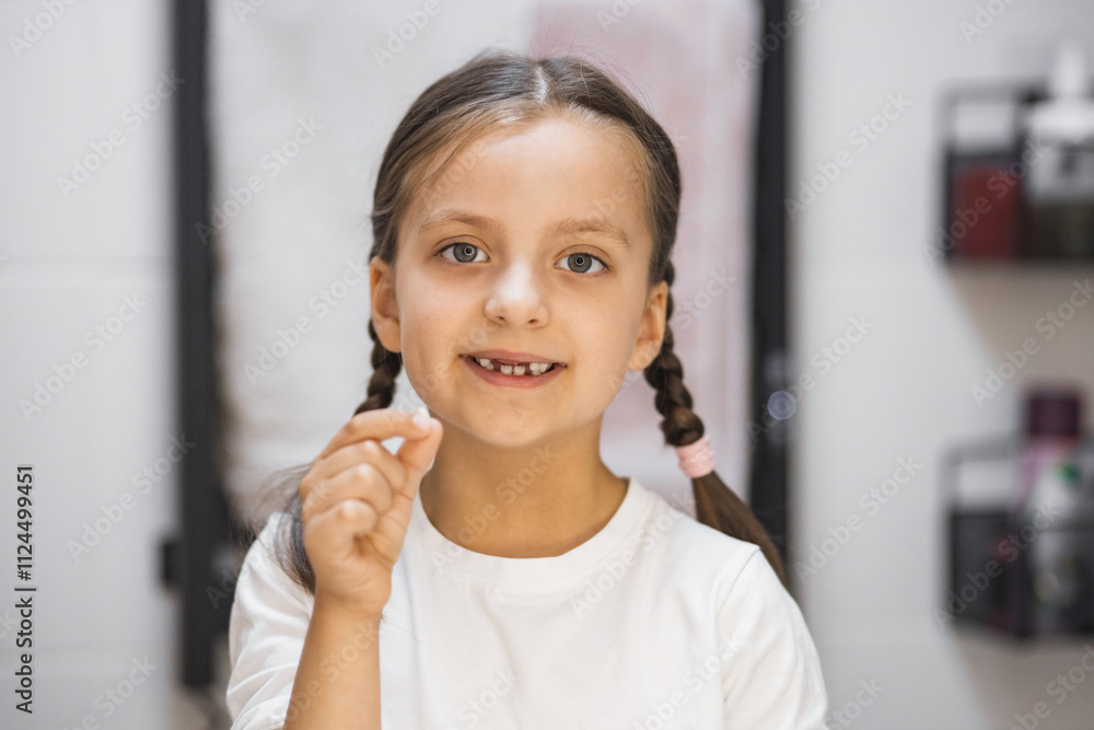 Portrait of young Caucasian girl holding baby tooth, smiling into bathroom mirror. Celebrating milestone of losing first tooth with happiness and curiosity. Bright eyes and braided hair. Portrait of young Caucasian girl holding baby tooth, smiling into bathroom mirror. Celebrating milestone of losing first tooth with happiness and curiosity. Bright eyes and braided hair.