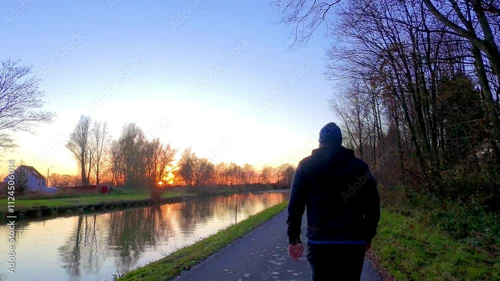 Enjoy a serene sunset stroll along a beautifully tranquil canal, which is surrounded by lush trees and nature Enjoy a serene sunset stroll along a beautifully tranquil canal, which is surrounded by lush trees and nature
