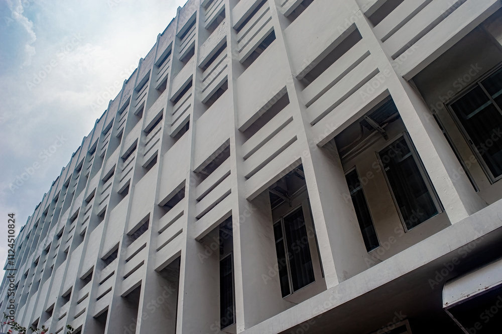 Fototapeta premium A modern, multi story building with a unique geometric facade featuring rectangular windows and concrete patterns, captured from a low angle against a cloudy sky