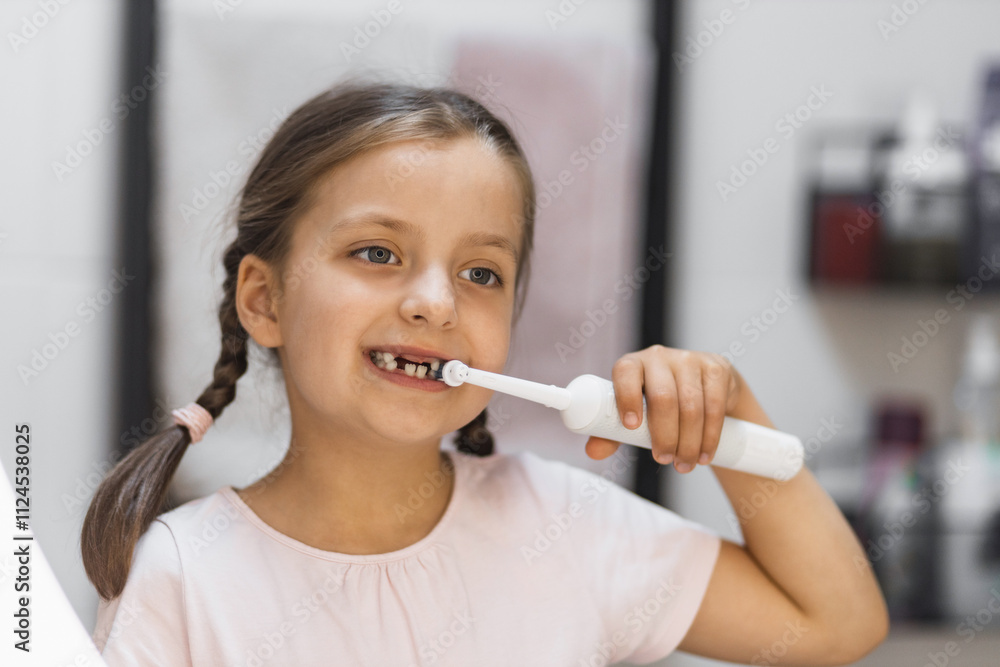 Little Caucasian girl with missing baby teeth brushing teeth with electric toothbrush in bathroom. Child looking into mirror while practicing oral hygiene and dental care. Little Caucasian girl with missing baby teeth brushing teeth with electric toothbrush in bathroom. Child looking into mirror while practicing oral hygiene and dental care.