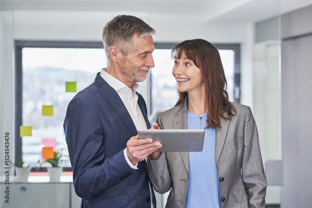 Happy mature businesswoman having discussion with colleague holding tablet PC in office Happy mature businesswoman having discussion with colleague holding tablet PC in office