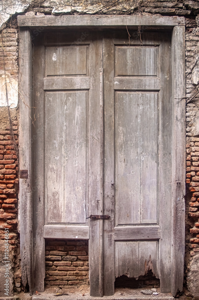 An old, weathered wooden door with peeling paint and visible damage at the bottom, set in a brick wall, showcasing the passage of time