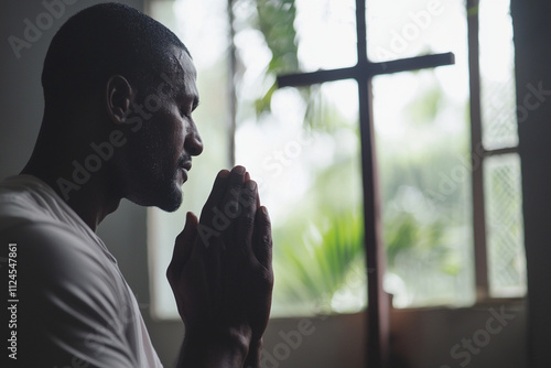 Man praying silently by a window illuminated by soft light