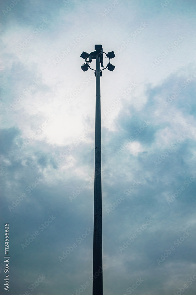 A tall street light pole with multiple floodlights against a cloudy sky, creating a dramatic and moody atmosphere A tall street light pole with multiple floodlights against a cloudy sky, creating a dramatic and moody atmosphere