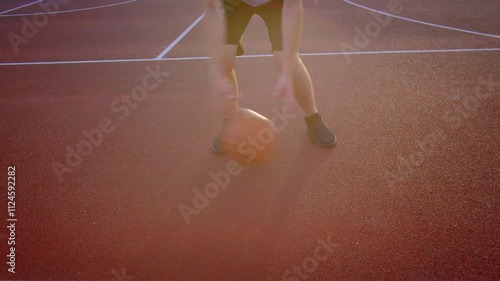 An athlete practices with a basketball on a sports court in the setting sun