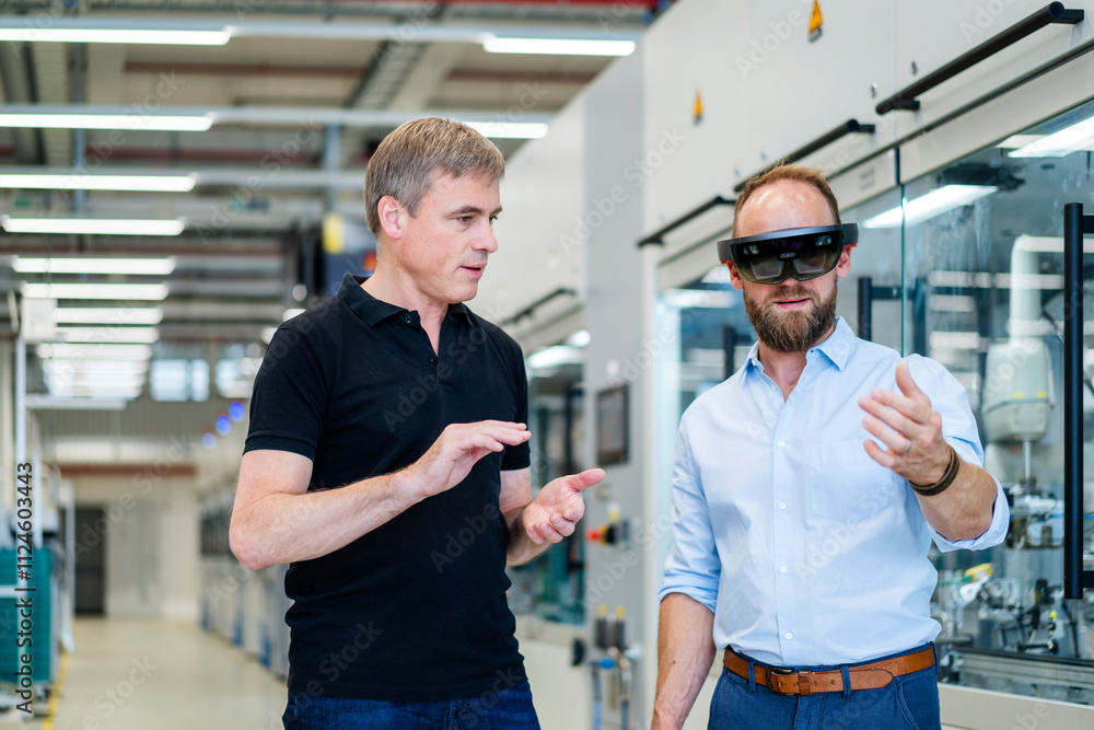 Technician wearing augmented reality glasses in a factory interacting with colleague Technician wearing augmented reality glasses in a factory interacting with colleague