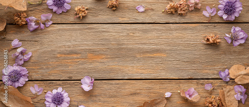 A rustic wooden background adorned with delicate purple flowers and dried leaves creates a charming, natural aesthetic.