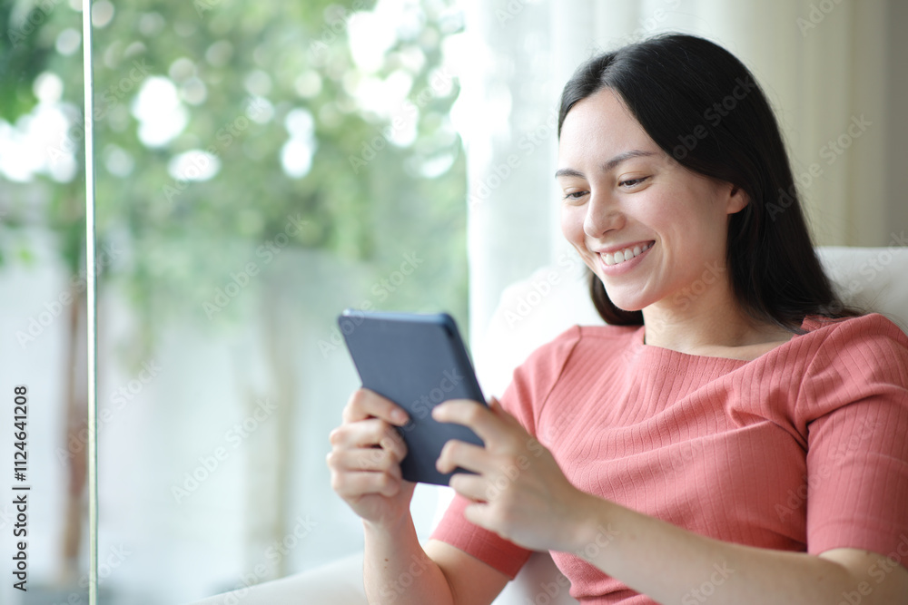 Happy asian woman reaidng ebook sitting at home Happy asian woman reaidng ebook sitting at home