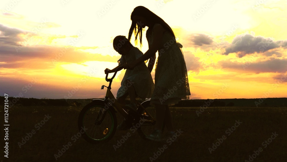 Fototapeta premium happy family. mother teaches little girl daughter ride bike sunset. concept happy family park. mom with child walks with bike park sunset sky. parent walks with kid together. happy childhood. girl