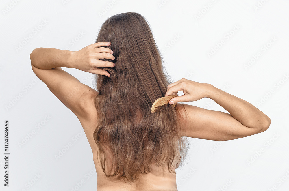 Adult lady, bare back, combing natural long hair with wooden comb on white background, isolated. Hair care. Adult lady, bare back, combing natural long hair with wooden comb on white background, isolated. Hair care.