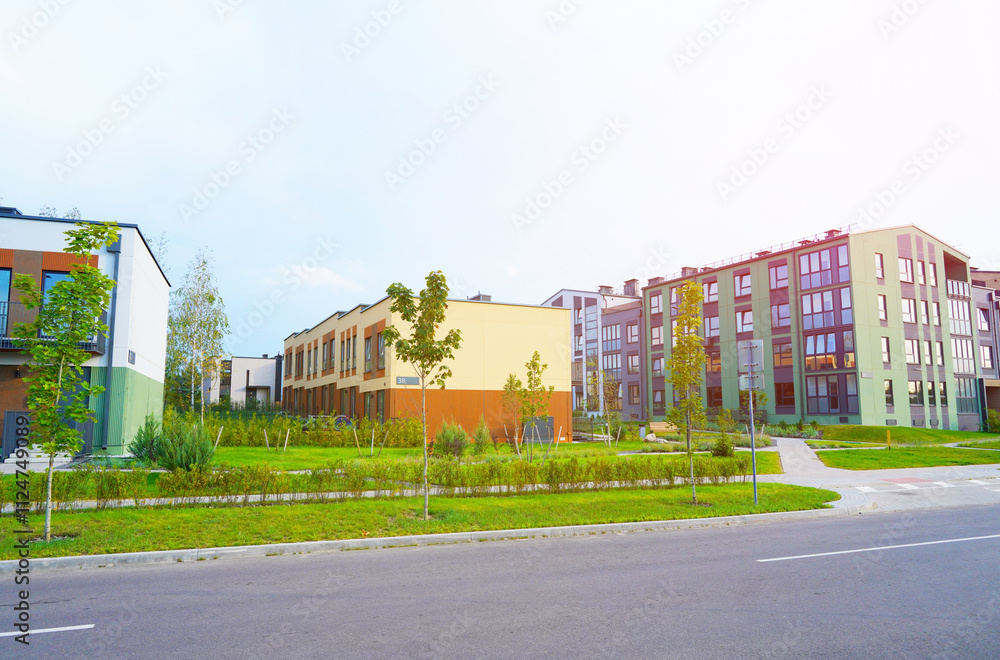 Fototapeta premium Townhouse in a suburb area. New apartment buildings in green enviroment. Street with Two-story townhouses. Modern Townhouse along sidewalk with green lawn. Pedestrian path with flowerbed shrubs.