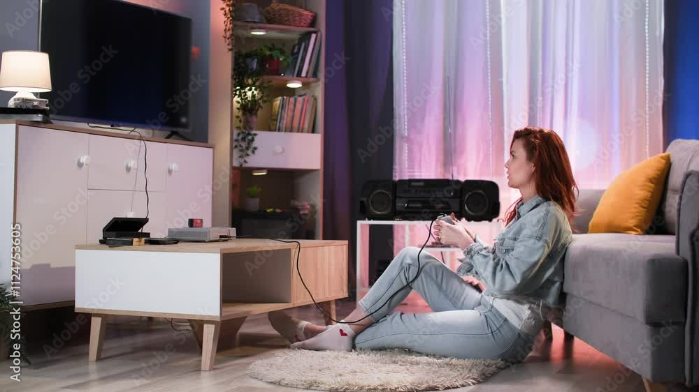 gamer, young woman with joystick in hands plays video games on TV sitting on floor near sofa in evening at home gamer, young woman with joystick in hands plays video games on TV sitting on floor near sofa in evening at home