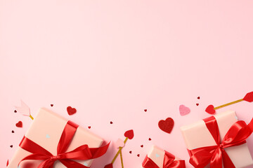 Valentine's Day pink gift boxes wrapped in red ribbons, surrounded by small red and pink hearts and Cupid's arrows on a pastel pink background. Lover, romance concept.