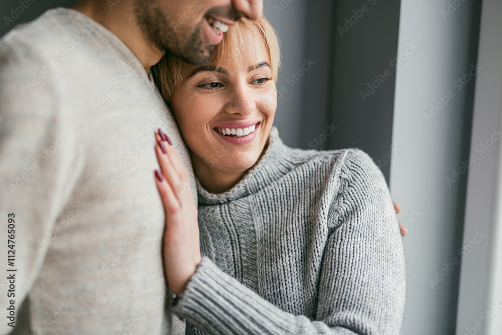Fototapeta premium A joyful and loving couple sharing a warm embrace while smiling. Both are wearing cozy sweaters, highlighting their happiness and affection.