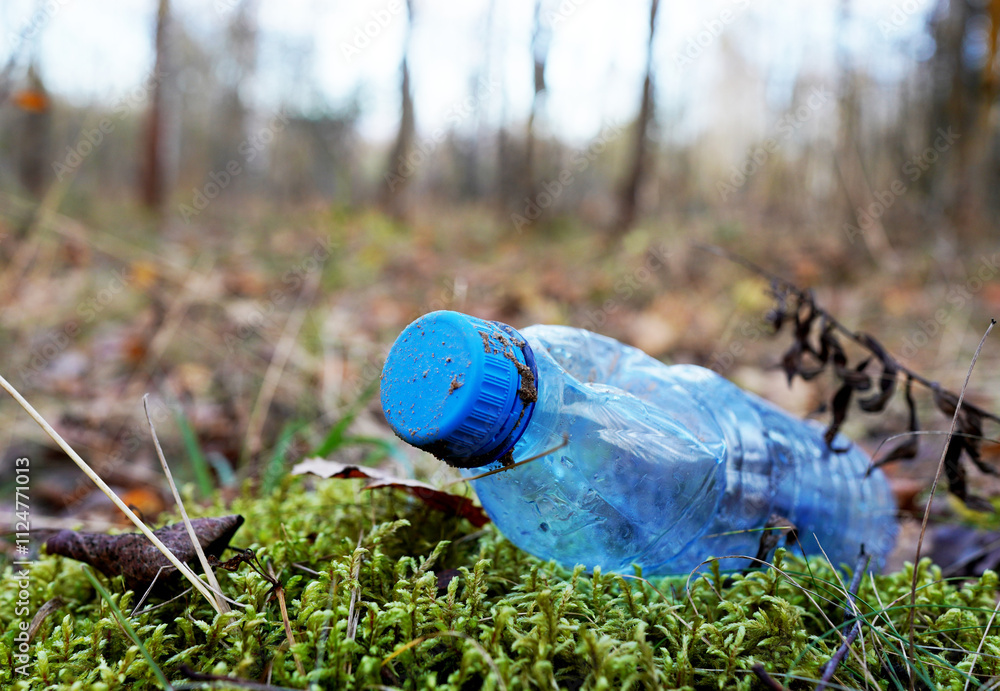 Obraz premium Plastic bottle thrown away in forest. Garbage in nature, reusable products. Rubbish thrown in forest. PET Plastic water bottle thrown out in nature. Waste in nature. Abandoned pet garbage waste.